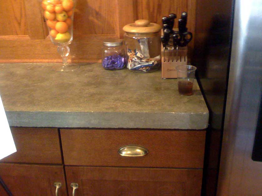 a table countertop of concrete with glass jars on it and brown cabinets below