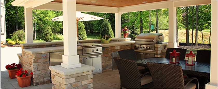 An outdoor kitchen in a plain area with dining chairs and table with a view of forest in front.