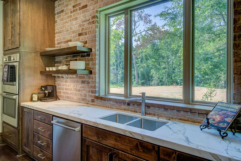 a white kitchen countertop option with brick wall and forest view from window
