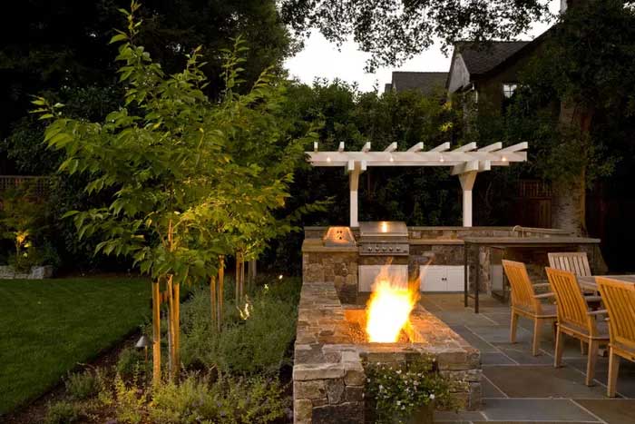 a fire place with dining and outdoor kitchen with grill along side of the garden.