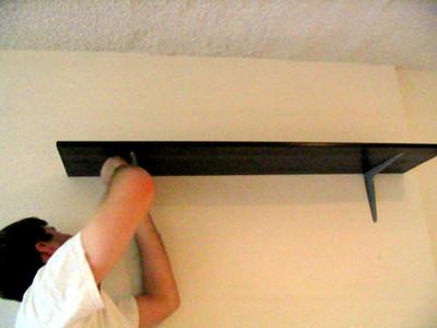 A person is installing a black-colored floating shelf for the kitchen.
