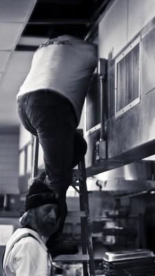 A worker is cleaning the kitchen exhaust hood in a kitchen from the inside.