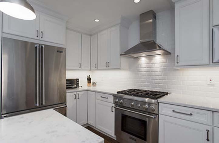 Full white designed kitchen with stainless steel hood and oven in the middle.