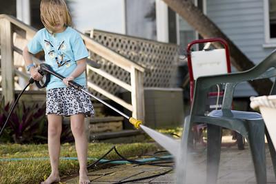 A child using the pressure washer to clean a chair outside the house.