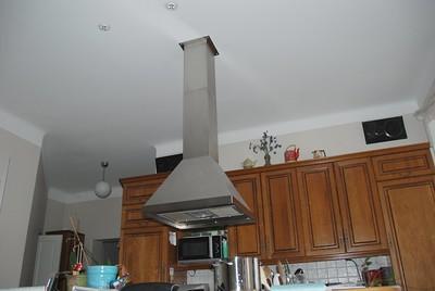A long kitchen exhaust hood in the center of a middle-sized kitchen with wooden cabinets across the wall.
