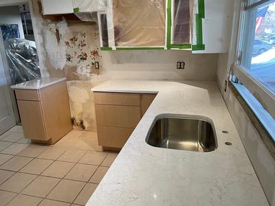 A small kitchen with white marble countertops and light brown wooden cabinets is being renovated. 