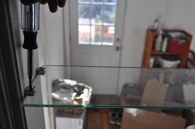 A floating shelf for kitchen made of glass is installed using a screw driver.