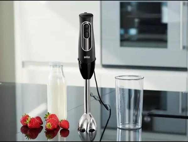 A modern immersion blender with a bottle of milk, a glass, and some strawberries is a small kitchen appliance.