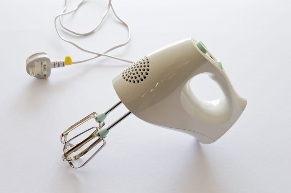 A white colored hand mixer placed on a countertop space with a wire, a great small kitchen appliance