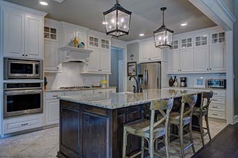 A modern kitchen with white colored cabinets and marble countertops.