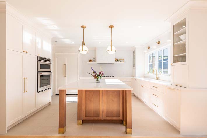 A properly lit kitchen with off-white shade and design. White wooden cabinets with a well-organized countertop space in the middle.
