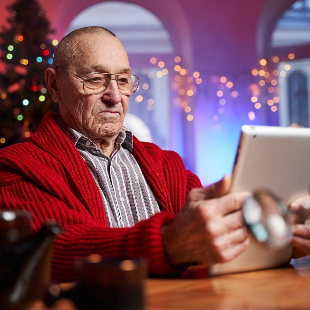 Serious elder man sitting at table with tablet in colourful room